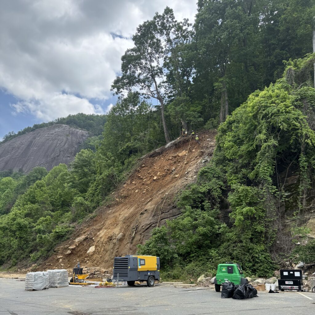 Crew in neon gear with drills, harnessed on landslide slope.